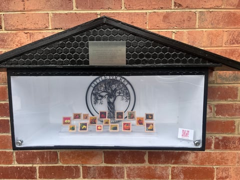 Wall-mounted display case with tree logo and colorful small items arranged below on a brick wall