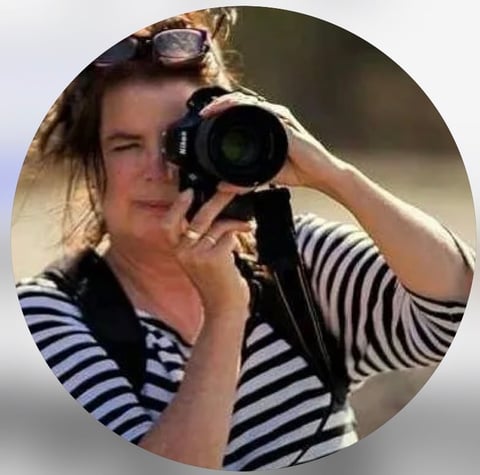 Woman in striped shirt holding a professional camera up to her face, photographing outdoors