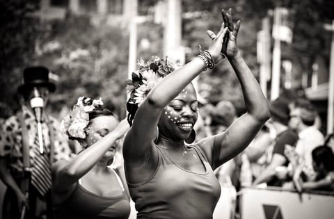Black and white photo of a woman with raised arms celebrating at a parade or public gathering with crowds in the background