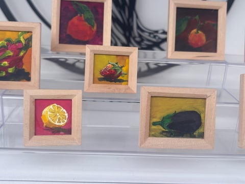 Collection of small framed fruit paintings in wooden frames displayed on a white shelf