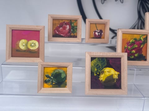 Collection of small framed paintings with wooden frames featuring colorful botanical and fruit still life artwork displayed on a white shelf